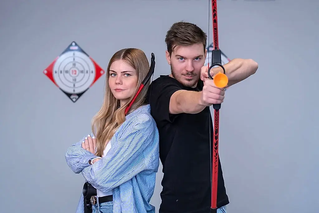 junge frau und maennlicher teilnehmer zielen mit pfeil und bogen auf zielscheiben bei der indoor bogenschiessen challenge.